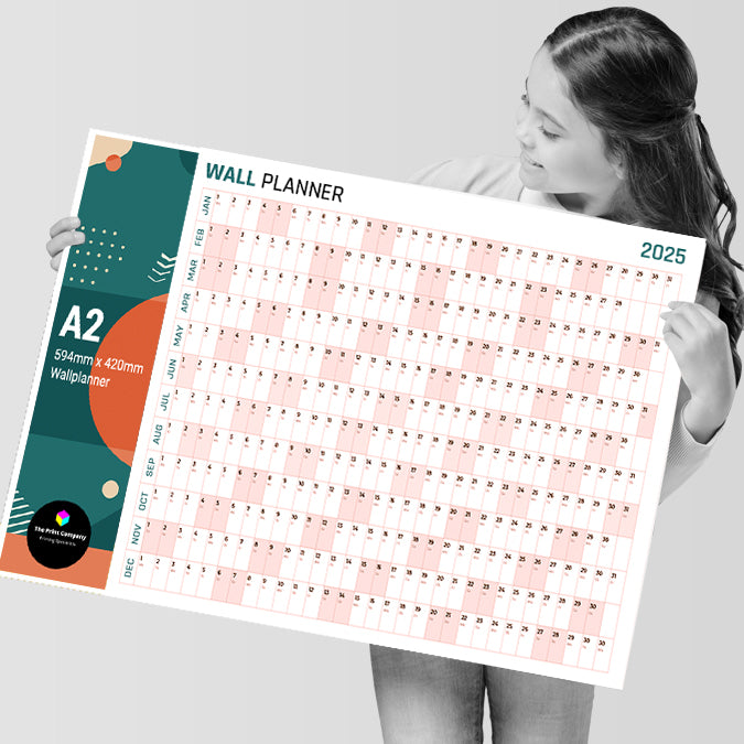 Smiling woman holding an A2 2025 wall planner, 594mm x 420mm, printed with a full-year grid and colourful header design